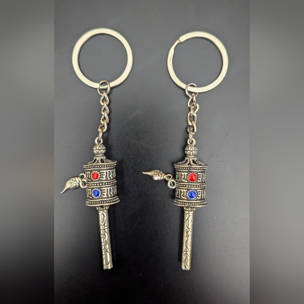 A Pair of Silver Prayer Wheel Keychains with Red and Blue Accents for Couples